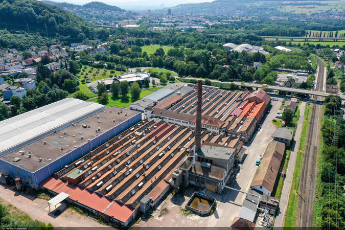 Das Lauffenmühle Areal von oben mit Industriegebäuden und Schornstein. Im Hintergrund die Stadt Lörrach