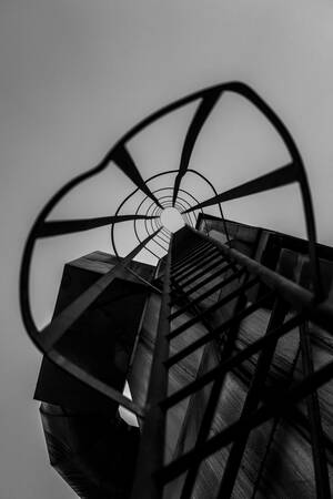 Eine schwarz-weiße Aufnahme zeigt eine Leiter auf der Lauffenmühle mit Käfigschutz, die in einen bewölkten Himmel führt.